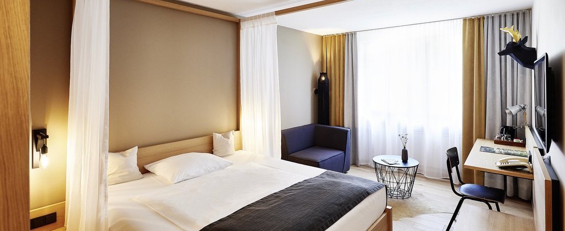 Helles Hotelzimmer mit Doppelbett, Sitzgelegenheiten und Schreibtisch.