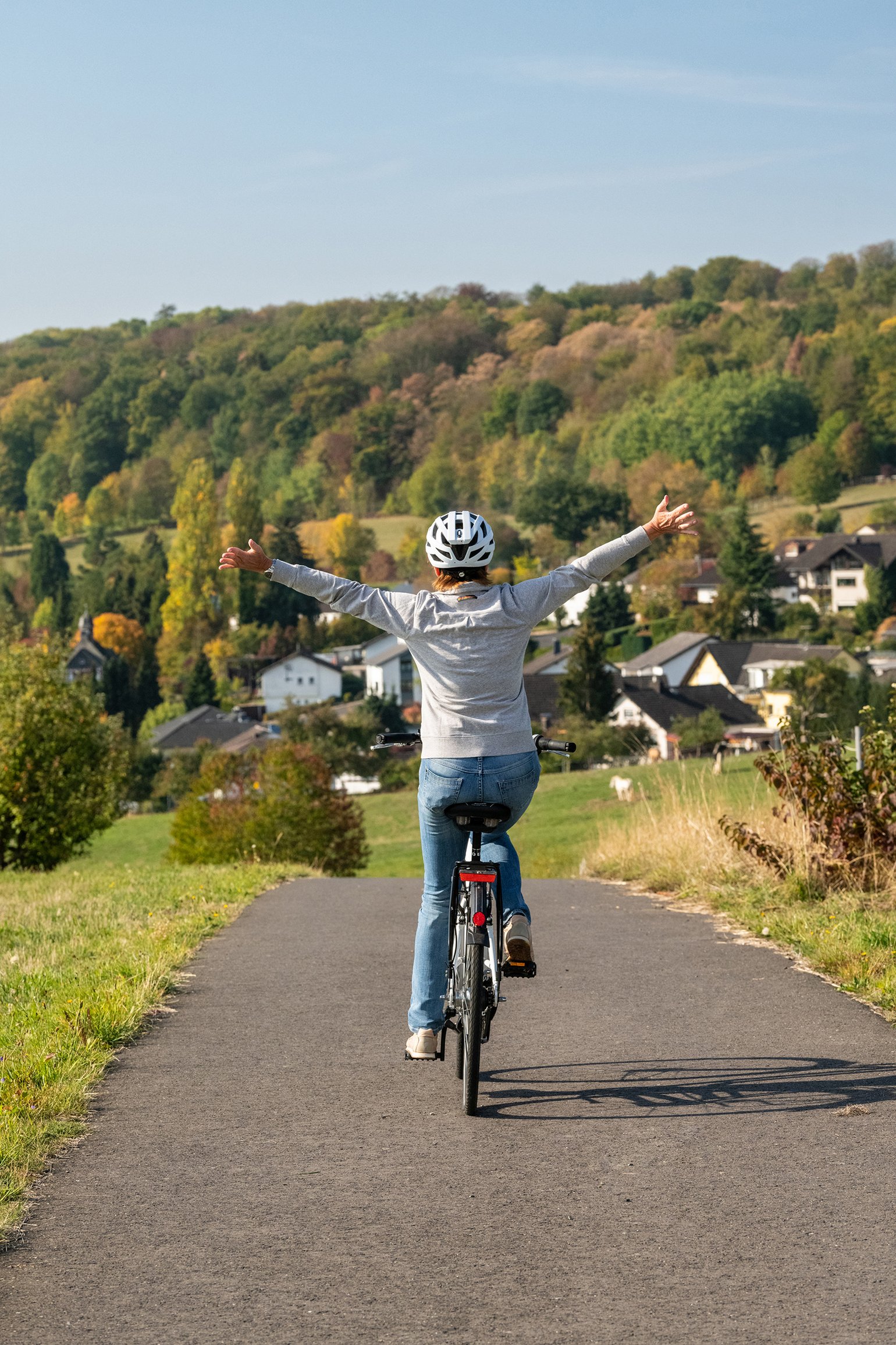 Frau fährt Fahrrad und breitet die Arme in der Landschaft aus