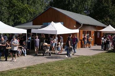 Besucher stehen vor einem Gebäude mit Zelten bei einer Veranstaltung