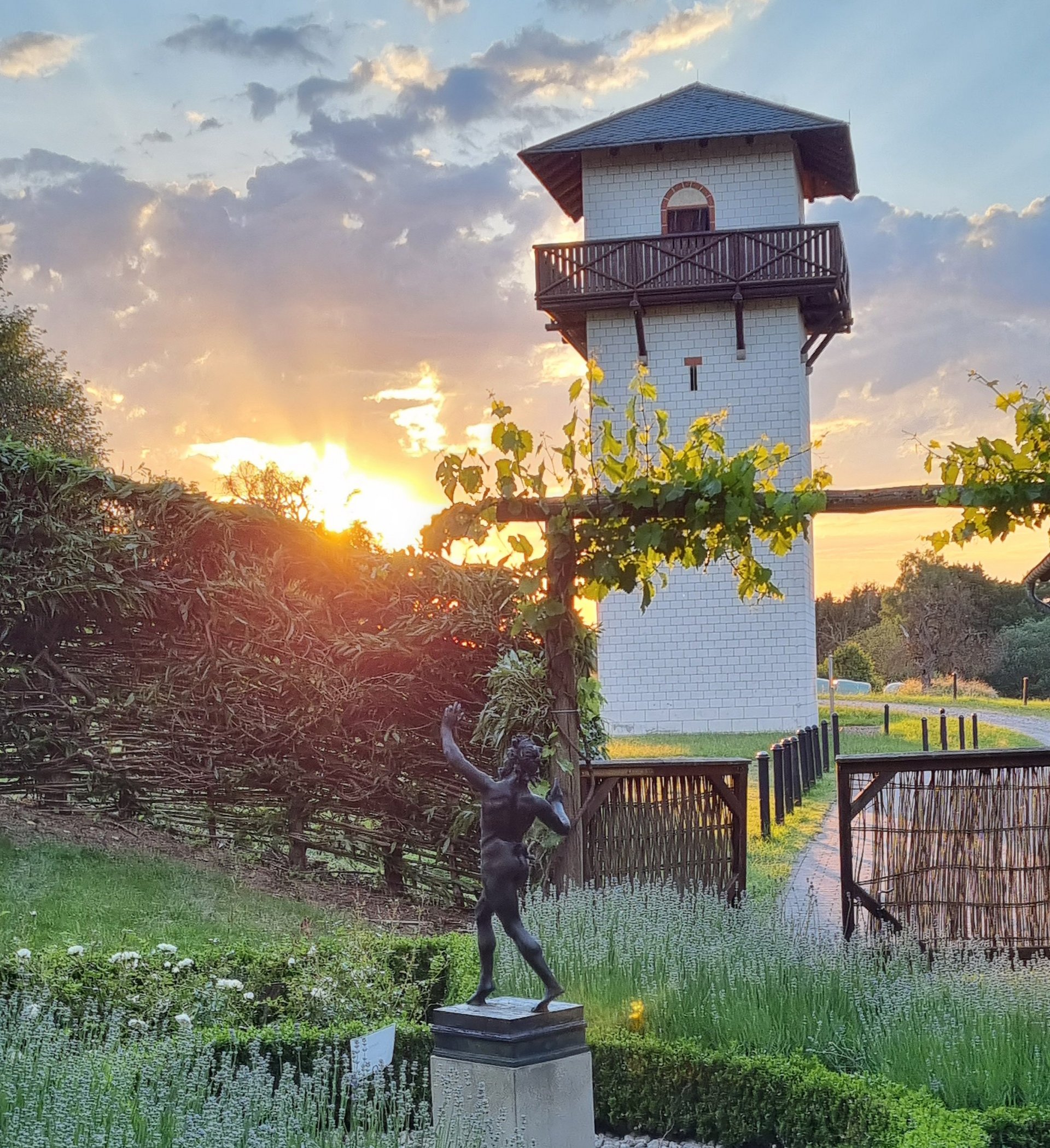 Eine Skulptur in einem Garten mit einem weißen Turm im Hintergrund bei Sonnenuntergang.
