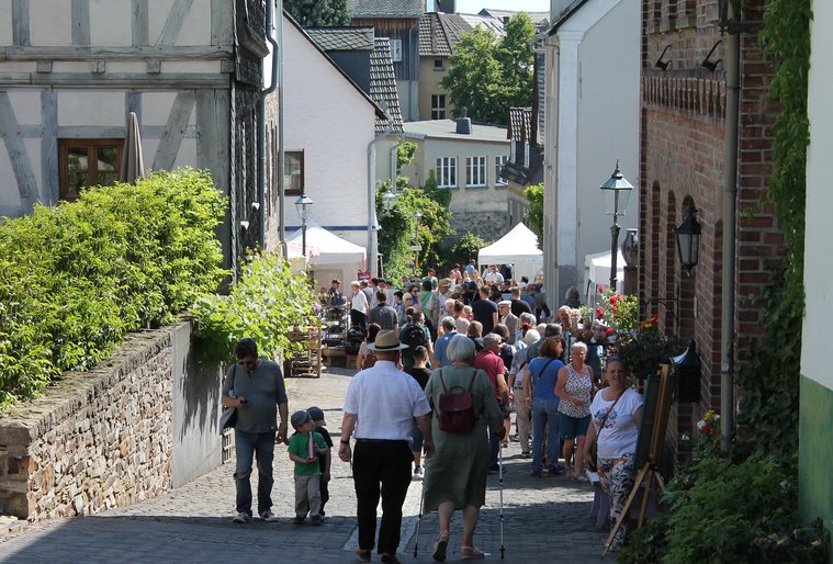 Menschen flanieren auf einer sonnigen Straße mit Marktständen.