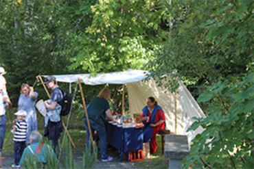 Besucher an einem Marktstand unter einem Zelt in einer grünen Umgebung