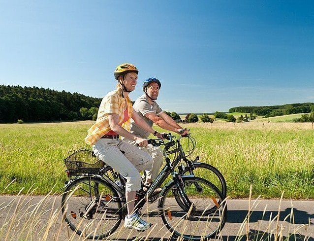 Zwei Radfahrer auf einem Radweg umgeben von grünen Wiesen