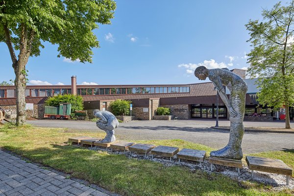 Zwei bildhauerische Figuren in einem Park mit einem Gebäude im Hintergrund