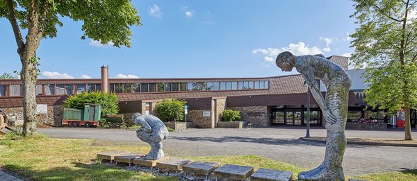 Zwei bildhauerische Figuren in einem Park mit einem Gebäude im Hintergrund