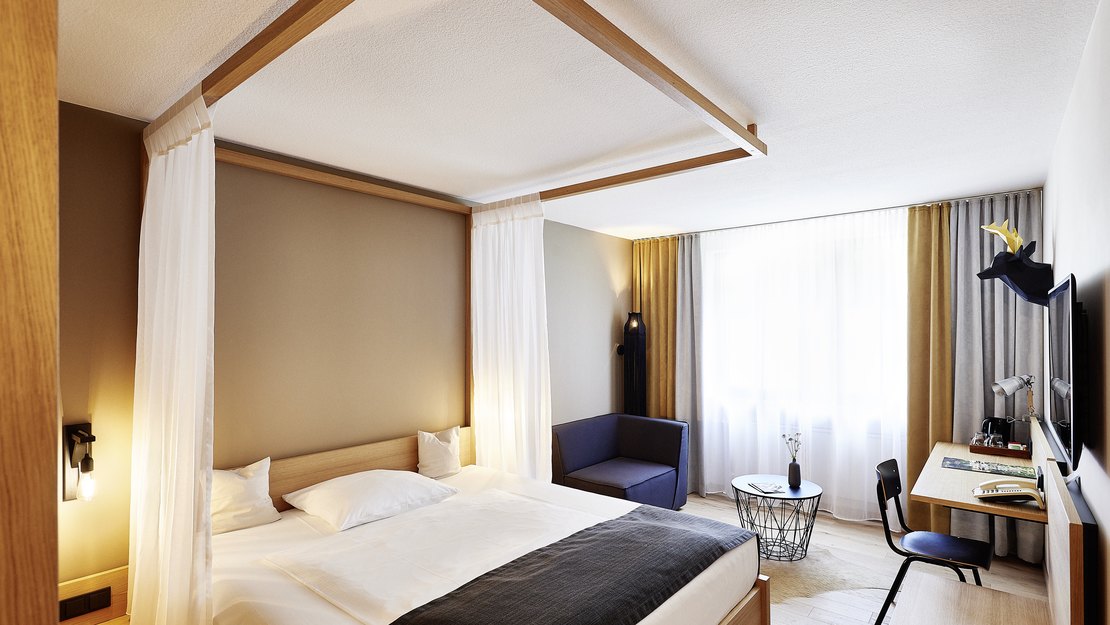 Helles Hotelzimmer mit Doppelbett, Sitzgelegenheiten und Schreibtisch.