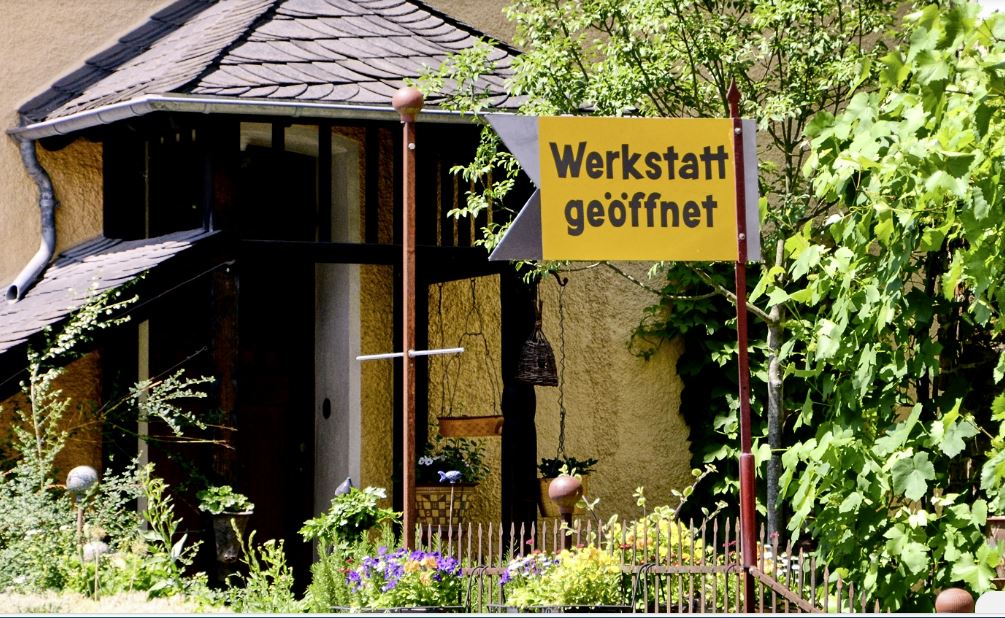 Schild zeigt an, dass die Werkstatt geöffnet ist, umgeben von Pflanzen