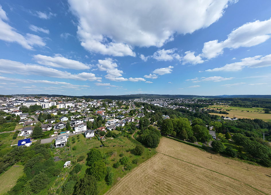 Luftaufnahme eines Dorfes mit Feldern und Bäumen unter bewölktem Himmel